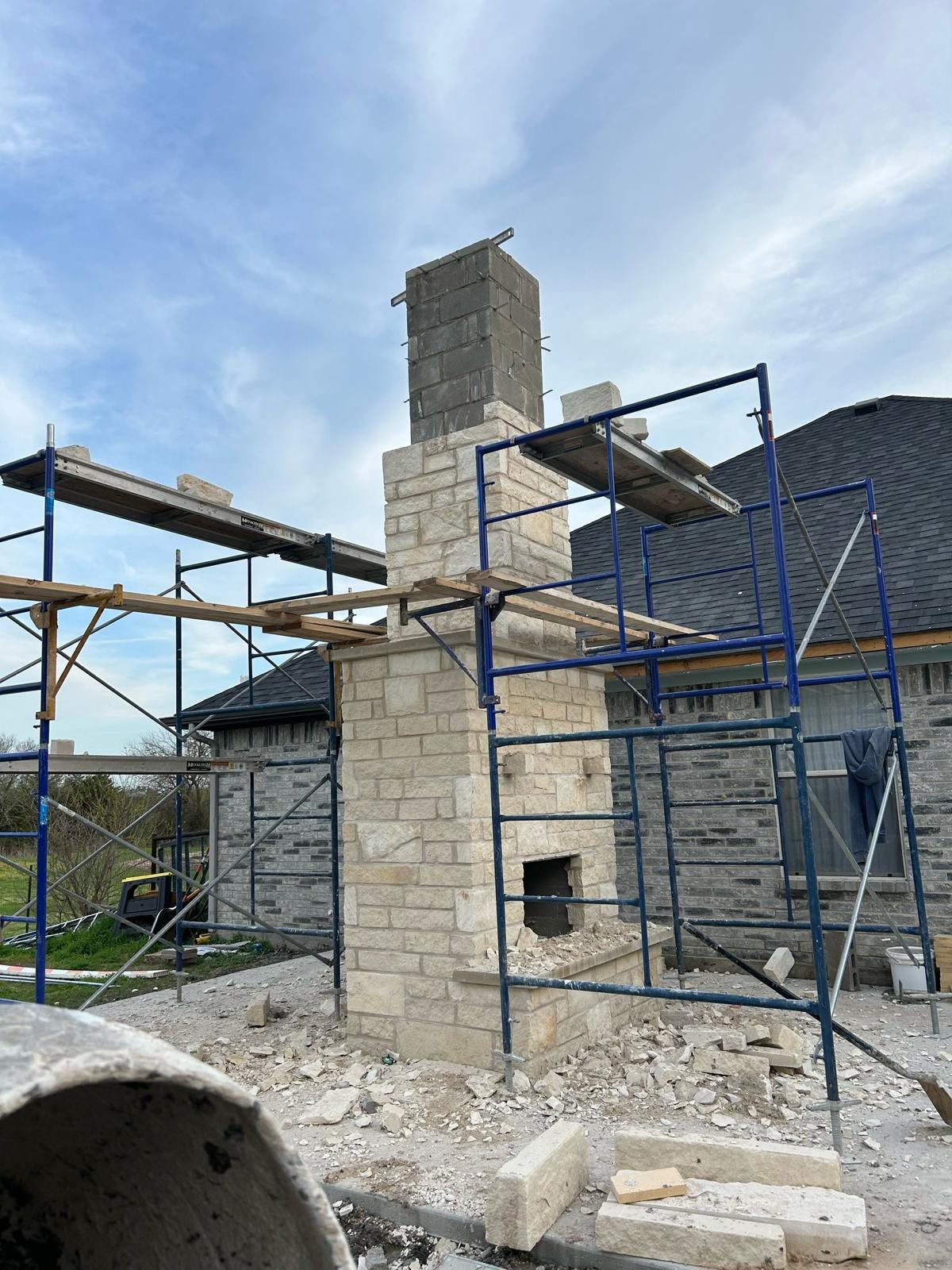 Tall masonry chimney under construction with scaffolding