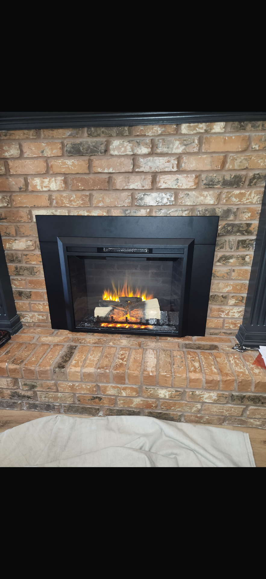 Black electric fireplace insert installed in a brick surround